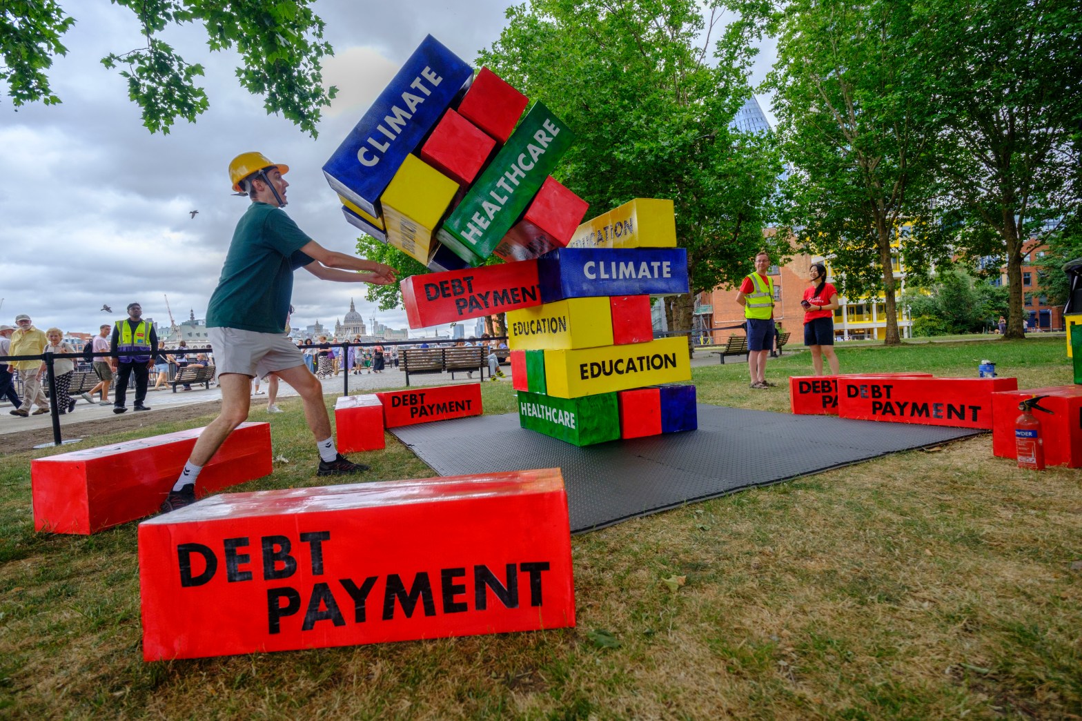 A giant Jenga game with blocks labelled Debt Payment, Education, Climate, Healthcare, etc.